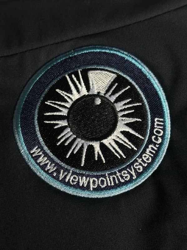 Detailaufnahme bestickter Viewpointsystem Patch in Aqua und Weiß auf dunklem Stoff
