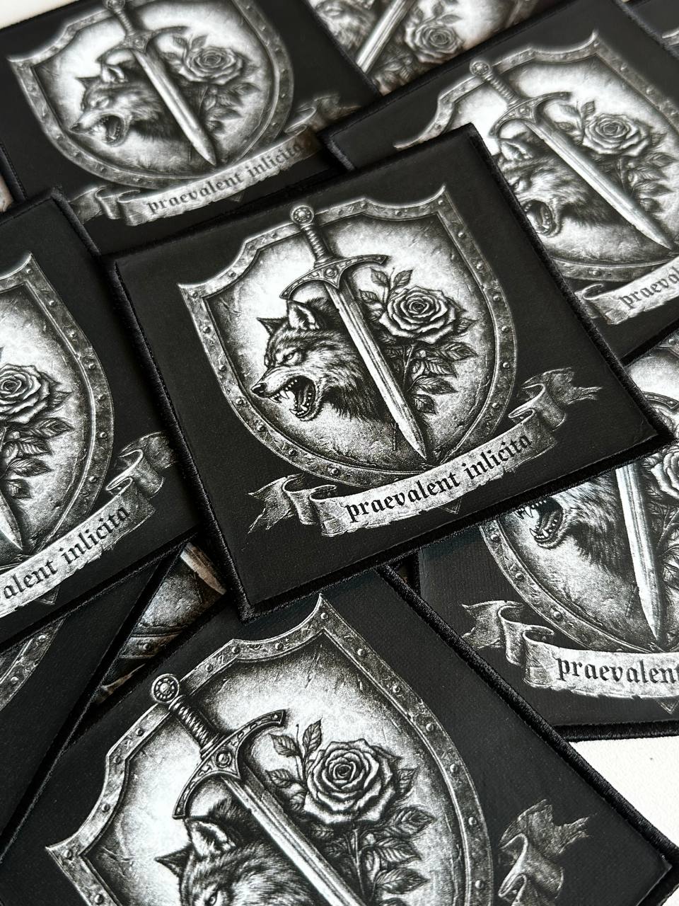 Mehrere gedruckte Aufnäher mit Wolf, Schwert und Rose Motiv und Schriftzug praevalent inlicita