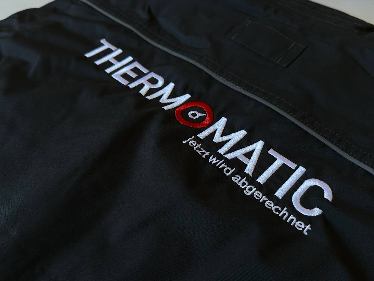 Thermomatic Logo gestickt in Weiß und Rot auf schwarzer Arbeitsjacke