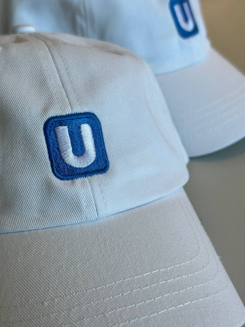 Caps besticken Wien: weiße Baseball Caps mit besticktem Wiener Linien U-Bahn Logo in Blau und Weiß